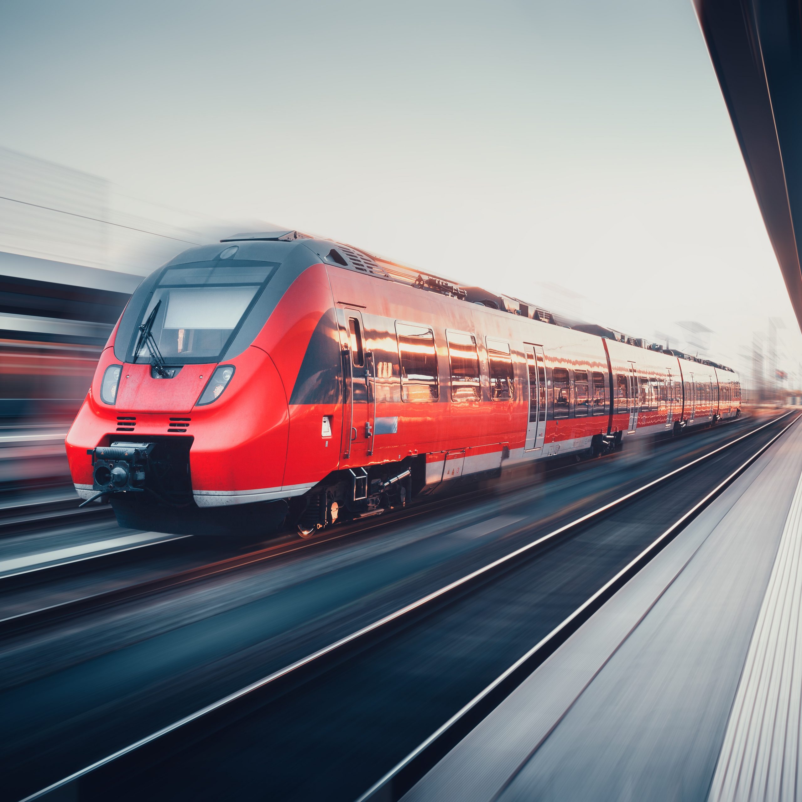 Beautiful railway station with modern high speed red commuter train with motion blur effect at sunset. Railroad. Vintage toning. Railroad travel background, tourism. Industrial